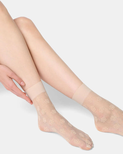 Sheer beige socks with floral patterns worn by a person on a light gray background