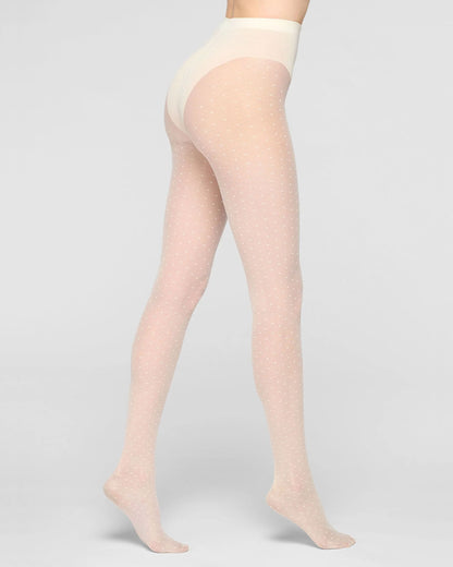 A model's lower body wearing sheer cream tights with a subtle dotted pattern, shown from a side-rear angle against a light gray studio background.