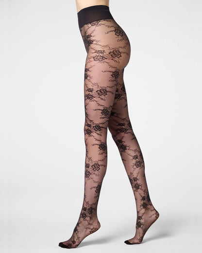 A model's legs wearing sheer black floral lace tights against a light gray studio background.