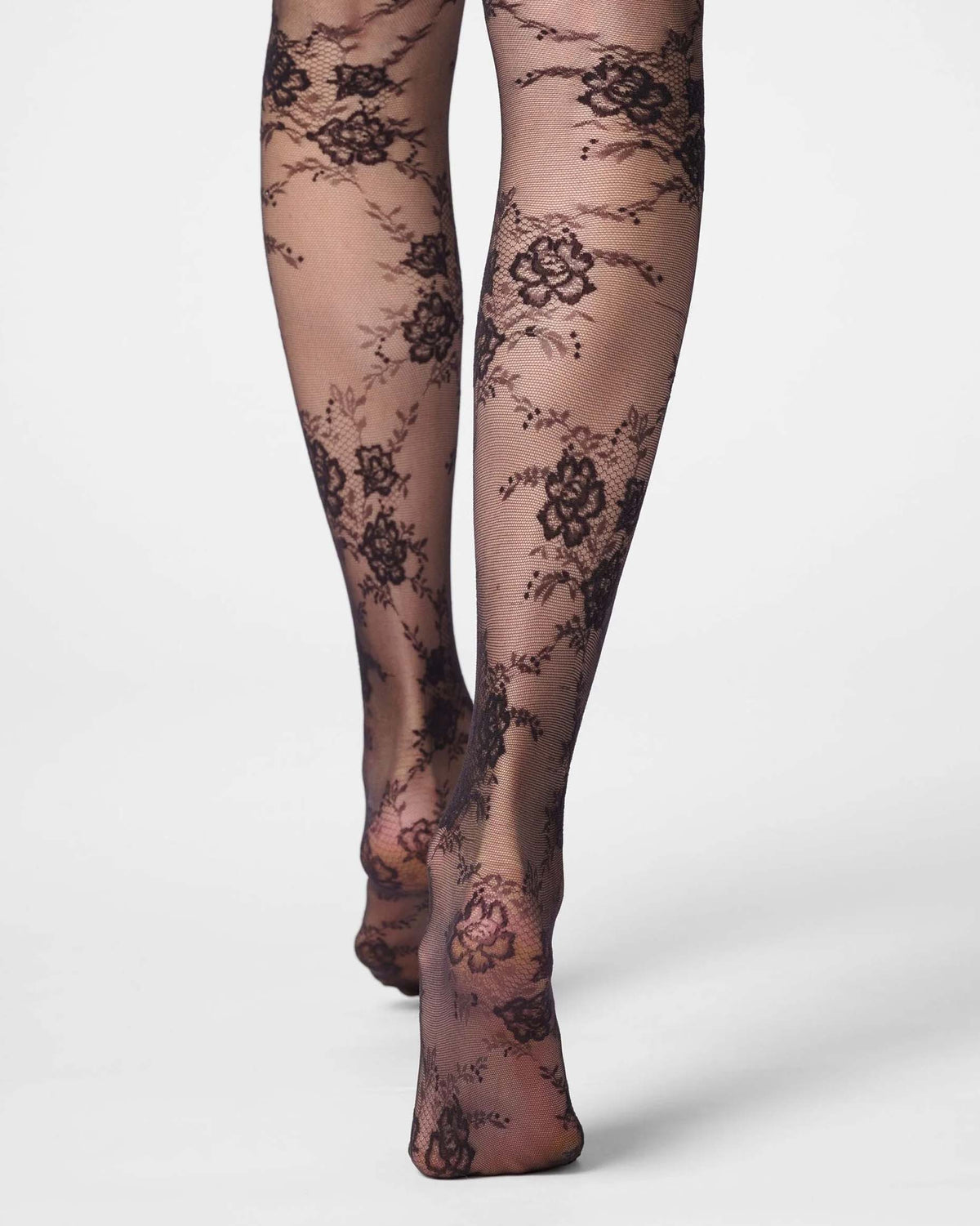 Black floral lace tights worn on legs, shown from the feet up against a clean light gray studio background.