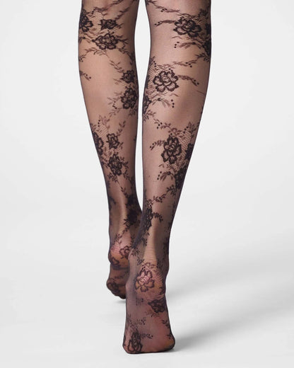 Black floral lace tights worn on legs, shown from the feet up against a clean light gray studio background.