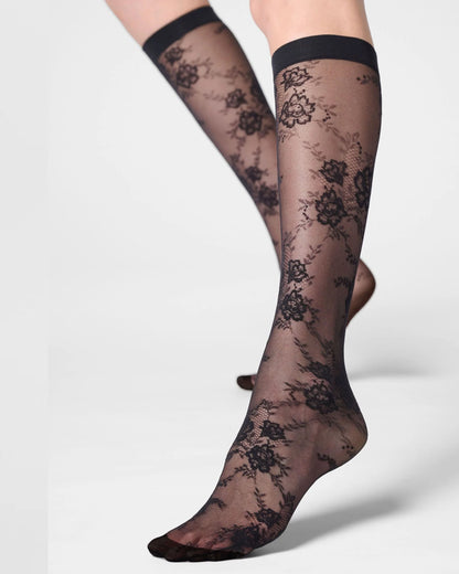 Black floral lace knee-high socks worn on legs, shown against a light gray studio background.