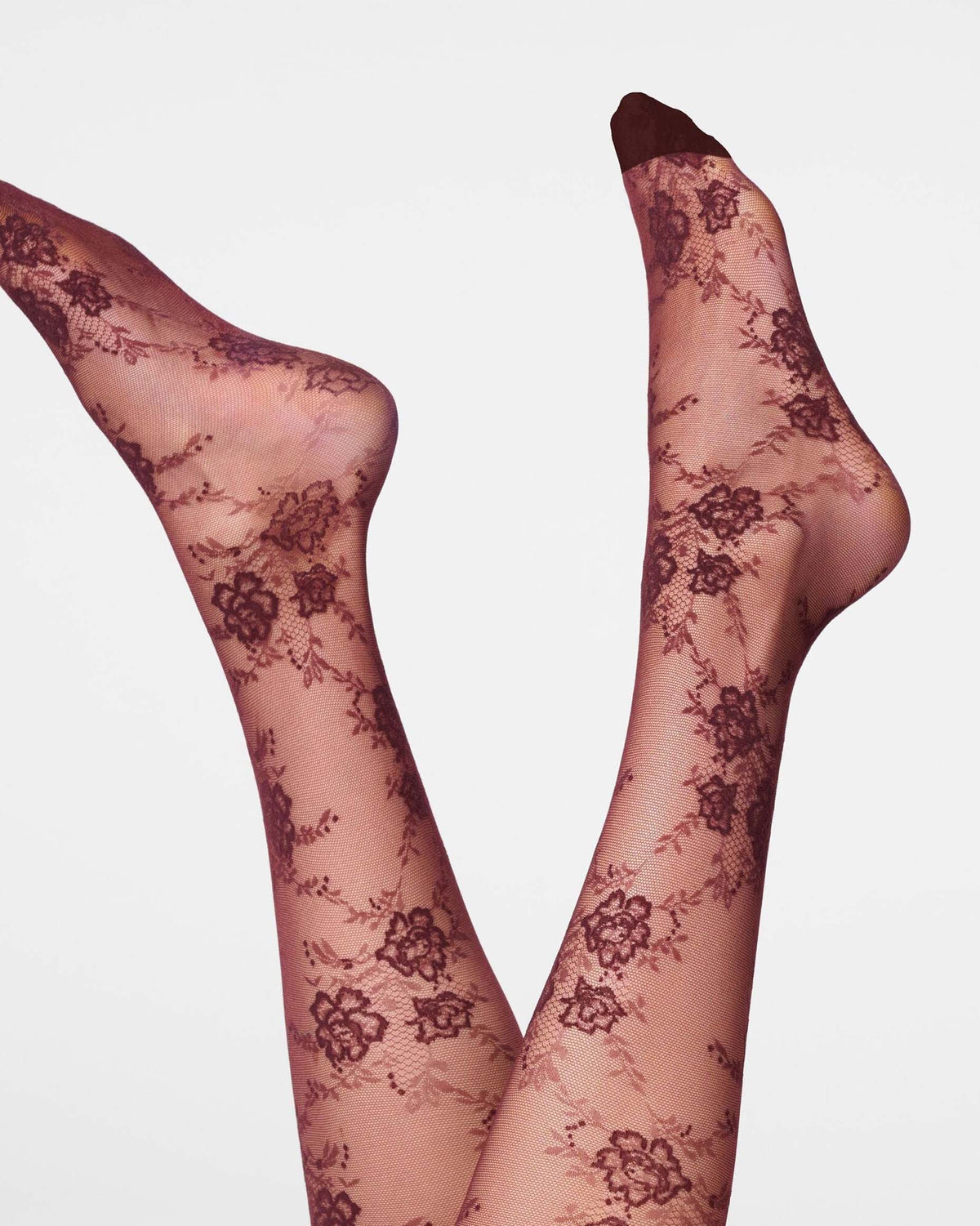 A pair of sheer burgundy floral lace tights worn on legs, shown against a plain light gray studio background.