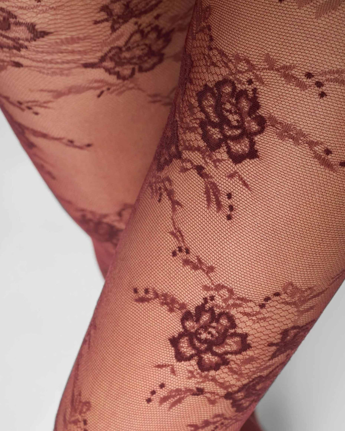 Close-up of sheer burgundy floral lace tights on a leg, showing embroidered floral motifs.