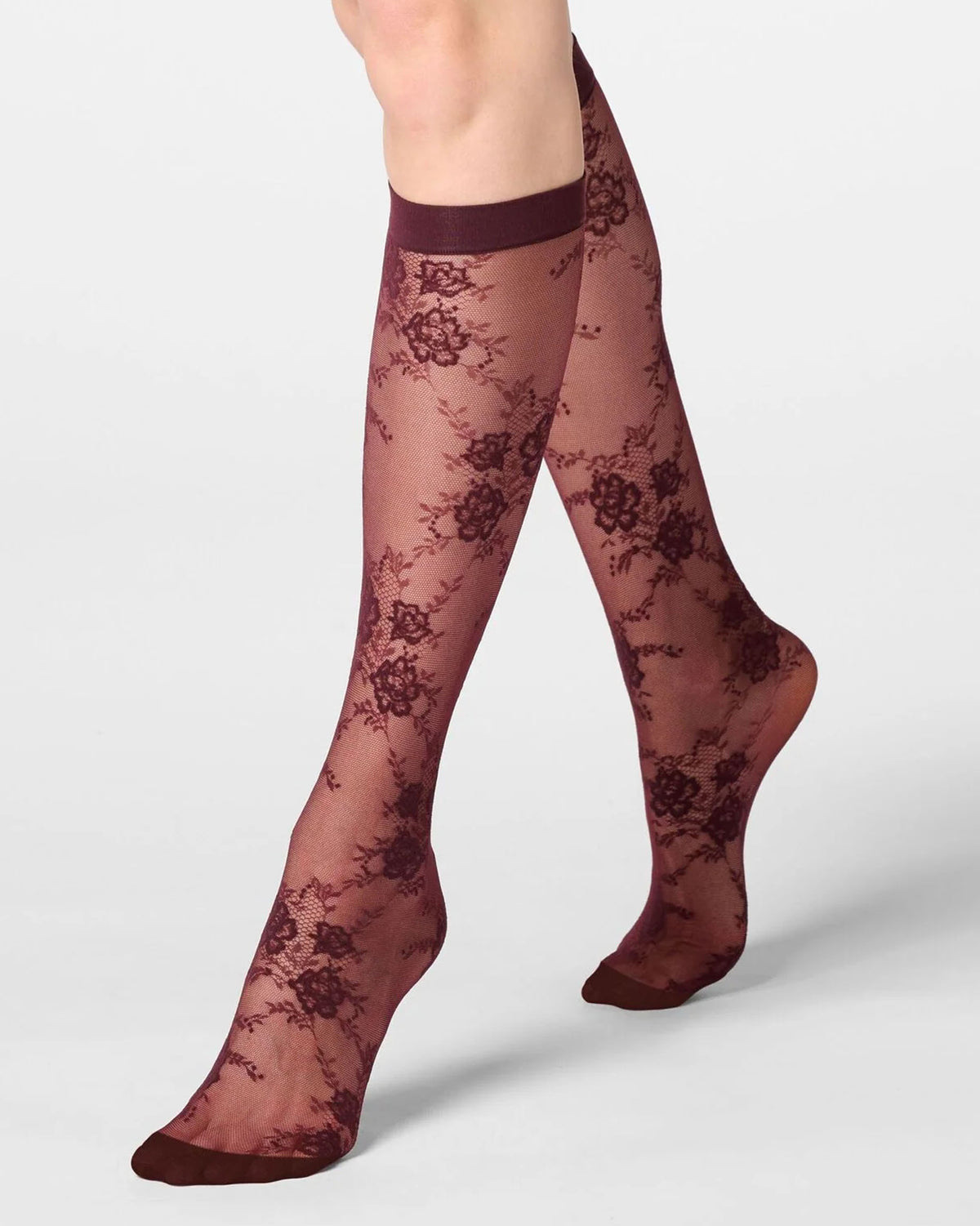 A pair of sheer knee-high lace socks in a wine color with a darker burgundy floral pattern, shown on a model's legs against a light gray studio background.
