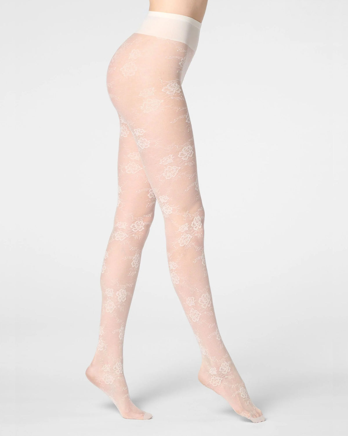 A model's legs wearing sheer cream tights with a delicate white floral lace pattern, shown from the waist down against a light gray studio background.