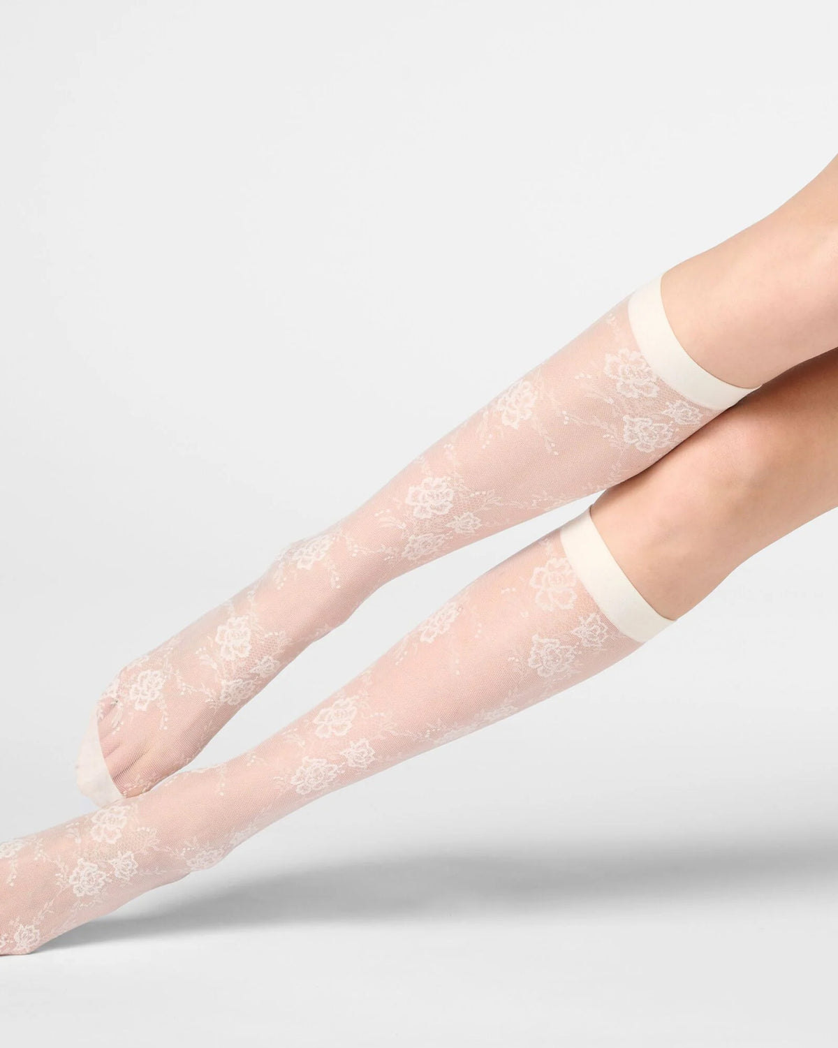 A pair of sheer off-white lace knee-high socks with solid cream cuffs, shown on a model's legs against a light gray studio background.