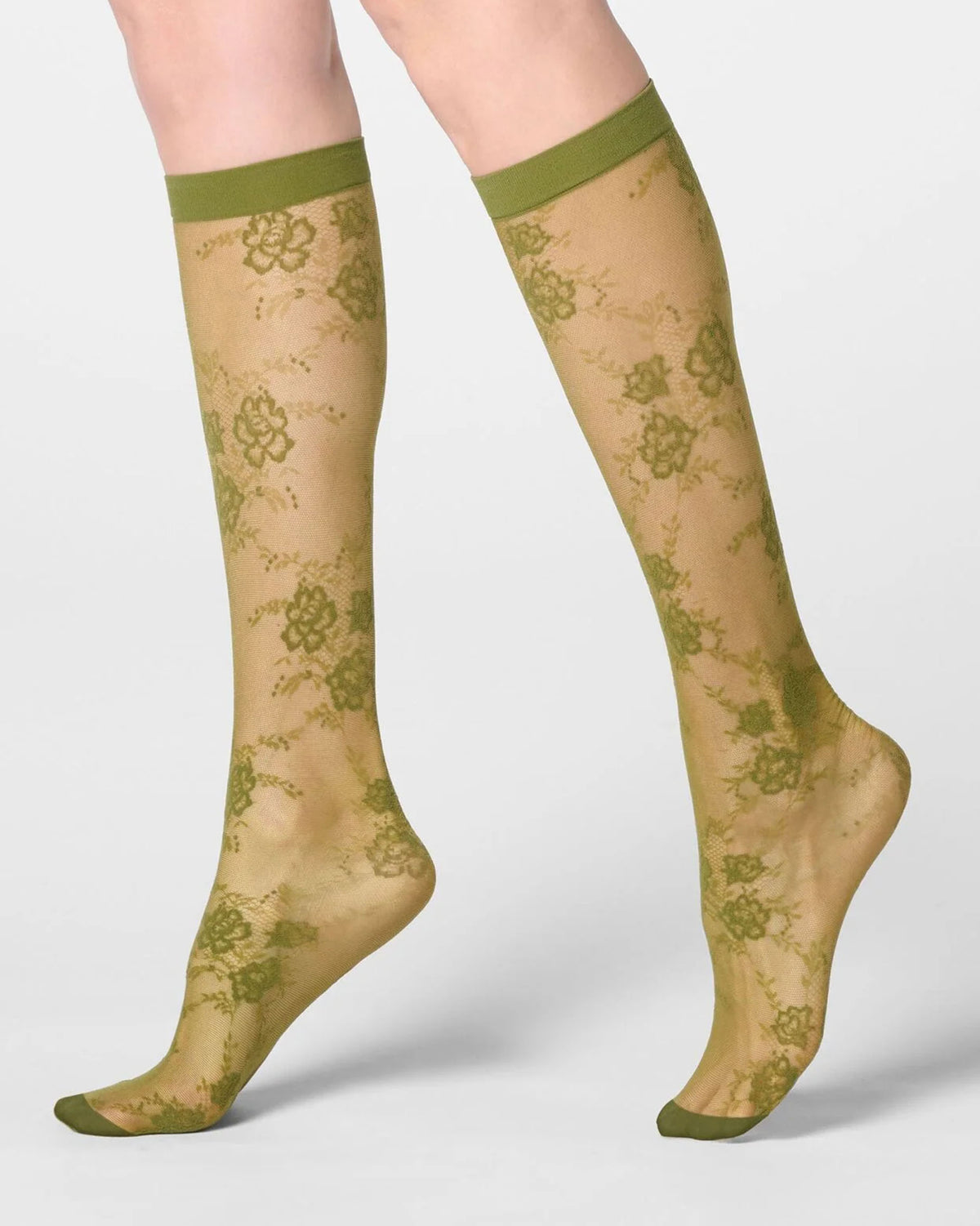 A pair of sheer knee-high socks with an olive green floral lace pattern and solid olive green cuffs, worn on a model's legs against a light gray background.