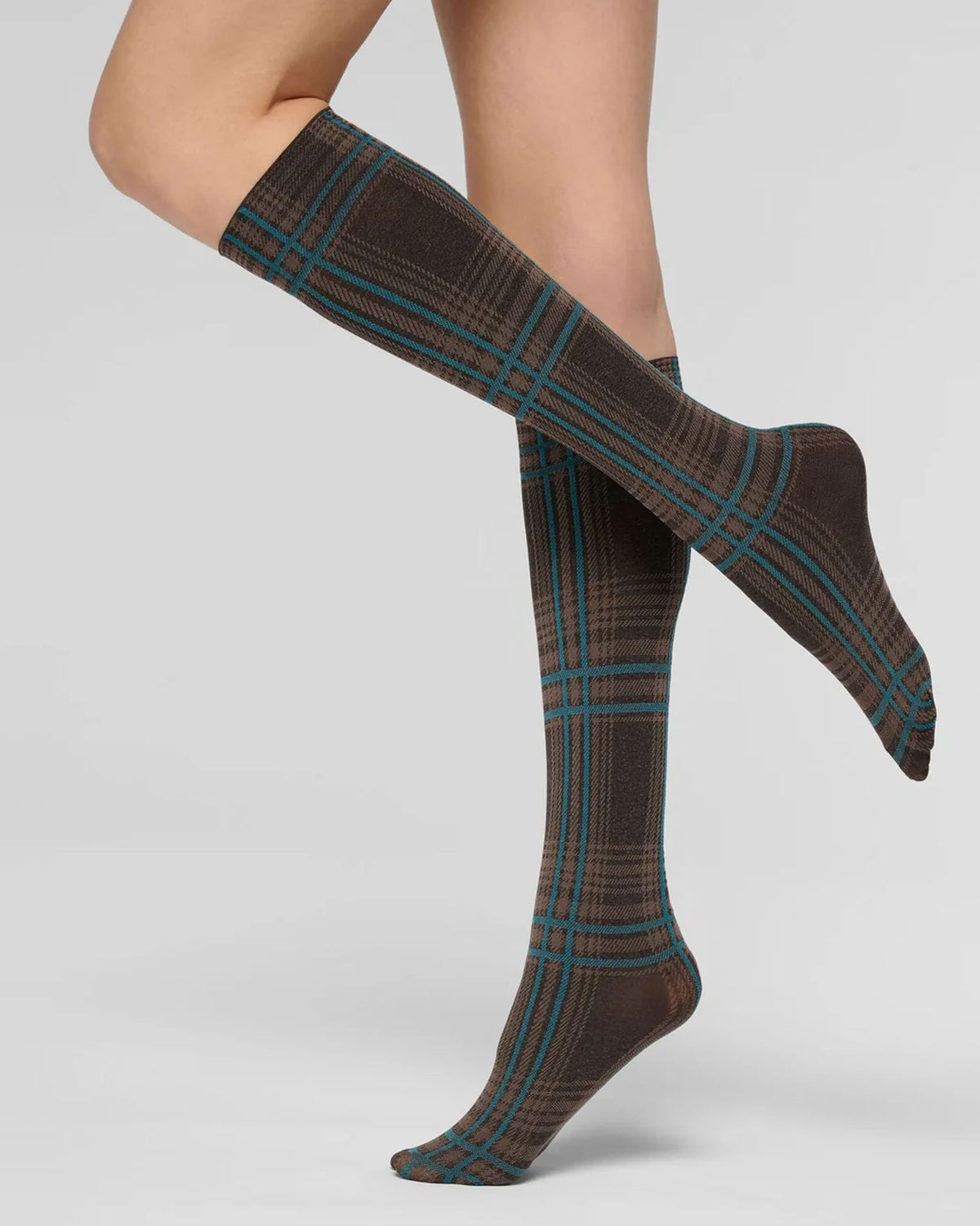 A pair of knee-high socks with a brown and beige plaid pattern accented by teal blue lines, shown on a model's legs against a light gray studio background.
