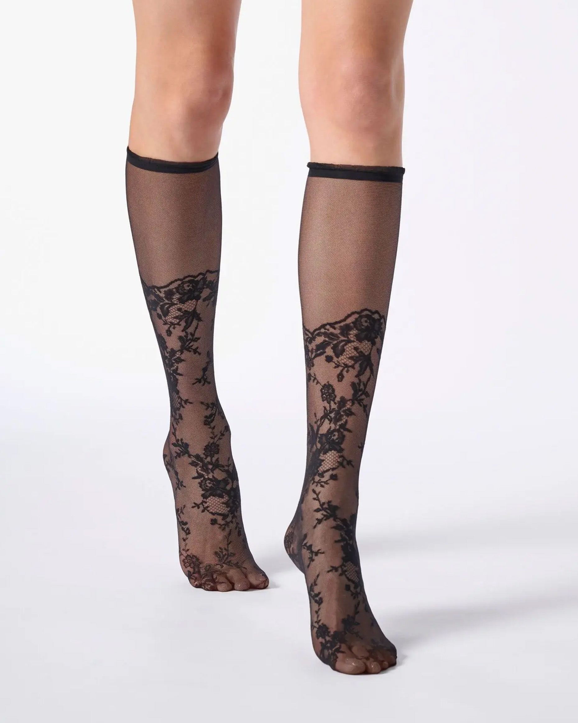 Sheer black knee-high socks with a floral lace pattern from the toe to the calf and a narrow cuff with ruffles.