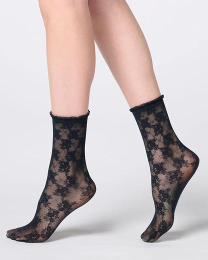 Black floral lace ankle socks worn on a model's feet, shown against a light gray studio background.