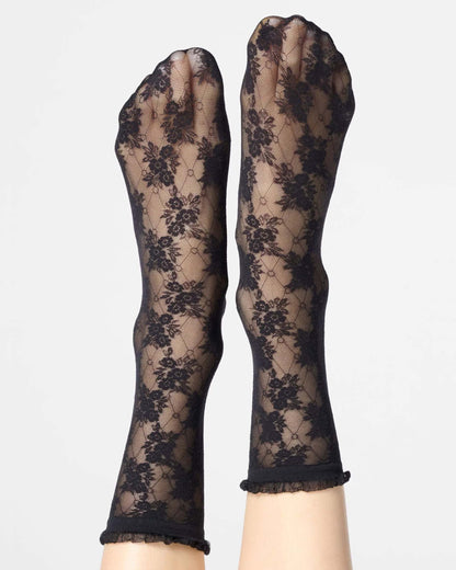 Black floral lace socks worn on feet, shown against a plain light gray background.