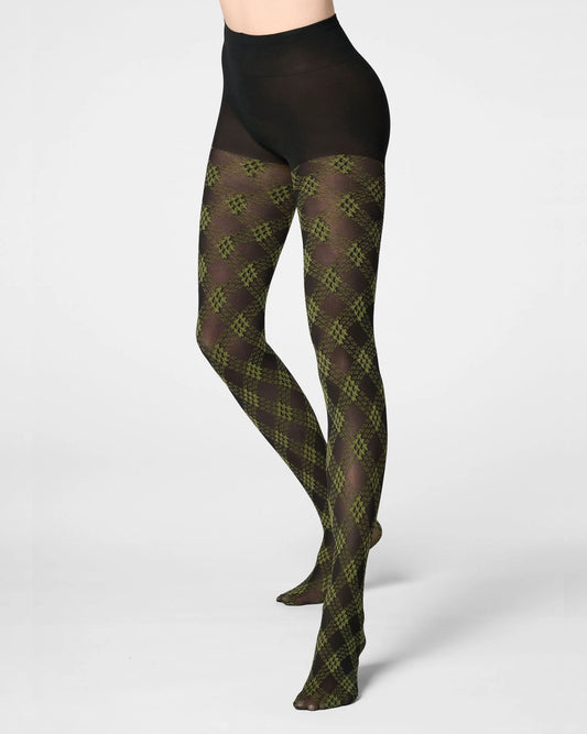 A model's legs wearing opaque black tights with an olive green and dark brown argyle pattern, shown against a light gray studio background.