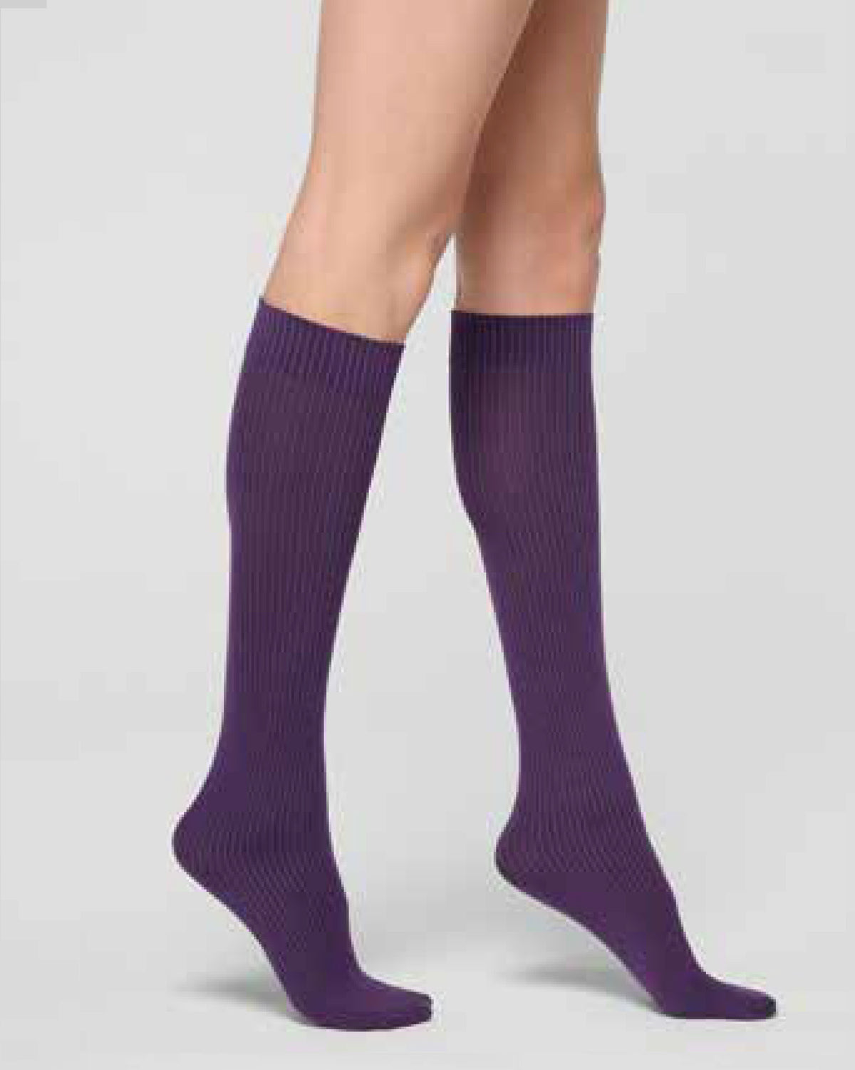 A pair of ribbed knee-high socks in a deep purple color, worn on a model's legs against a light gray studio background.