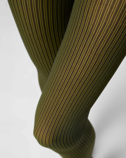 Close-up of ribbed tights with vertical olive green and black stripes, shown on a person's legs against a light gray background.