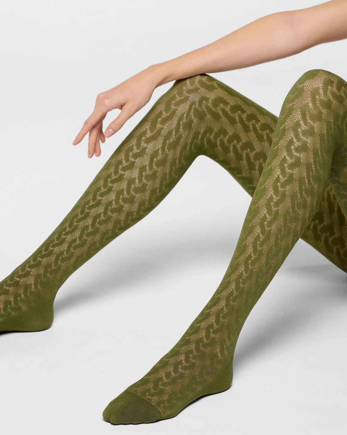 A model's legs wearing olive green hosiery with a textured, wavy pattern, posed against a light gray studio background.
