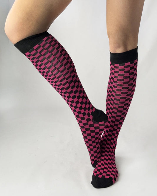 Knee-high socks with pink and black checkered pattern worn by a person on a light gray background