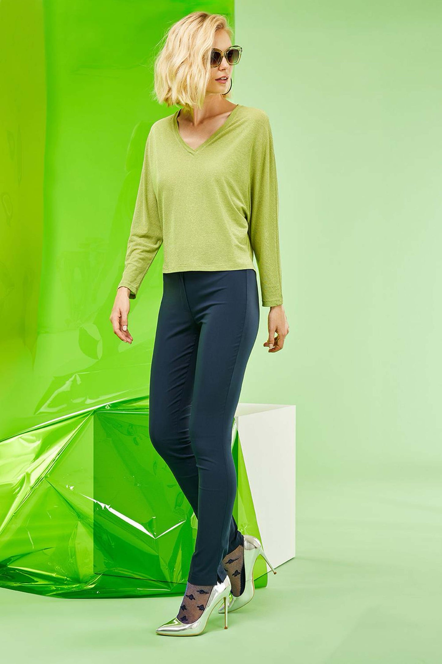 SiSi Belt Treggings - Navy blue light weight high waisted stretch viscose trouser leggings (treggings), with 2 buttons and zip closure and matching belt. Worn by a female model with short blonde hair, sunglasses, lime green top, sparkly socks and silver stiletto heels.