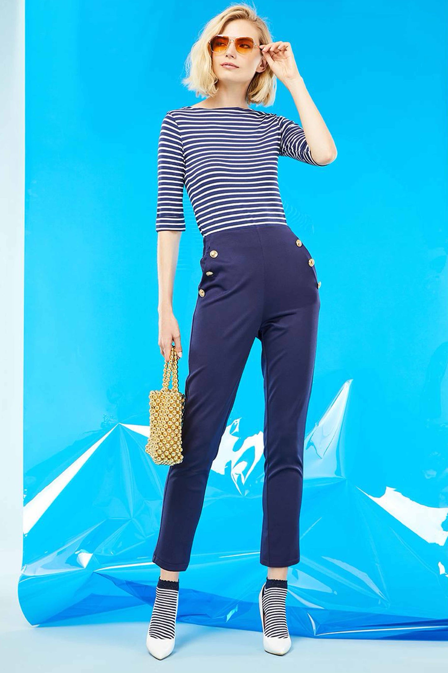 SiSi Brigitte Trouser - High waisted navy blue trouser leggings with elasticated waist band on the back, side pockets and big gold button details along the pockets. Worn with a stripe top, low ankle socks and white high heels.
