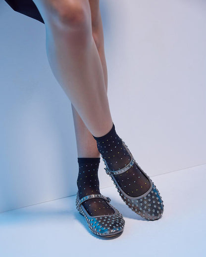 Person wearing black studded flats and black socks on a white background