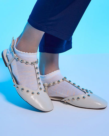 White studded shoes worn with white socks on a blue background