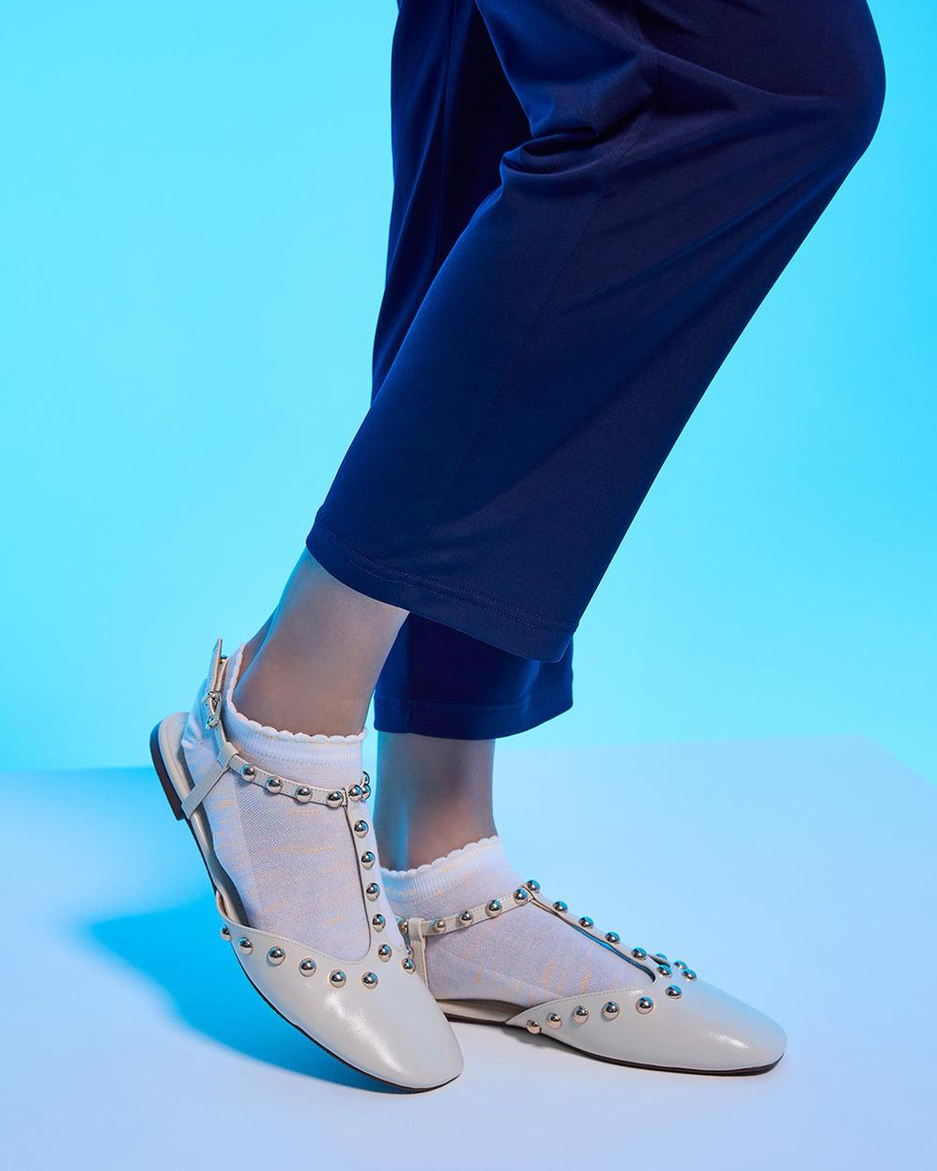 White studded shoes worn with blue pants on a blue background