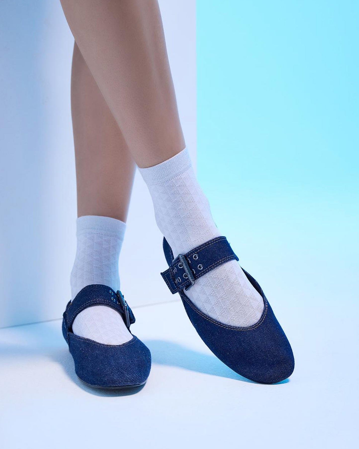 Blue shoes with buckles worn with white socks on a light blue background