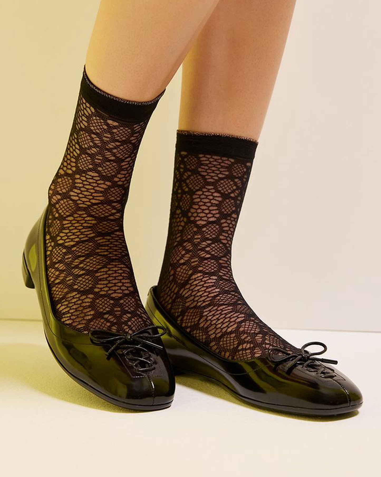 Sheer black micro mesh fashion ankle socks with a circular floral style pattern, plain cuff with a sparkly silver edge, worn with a black pump.
