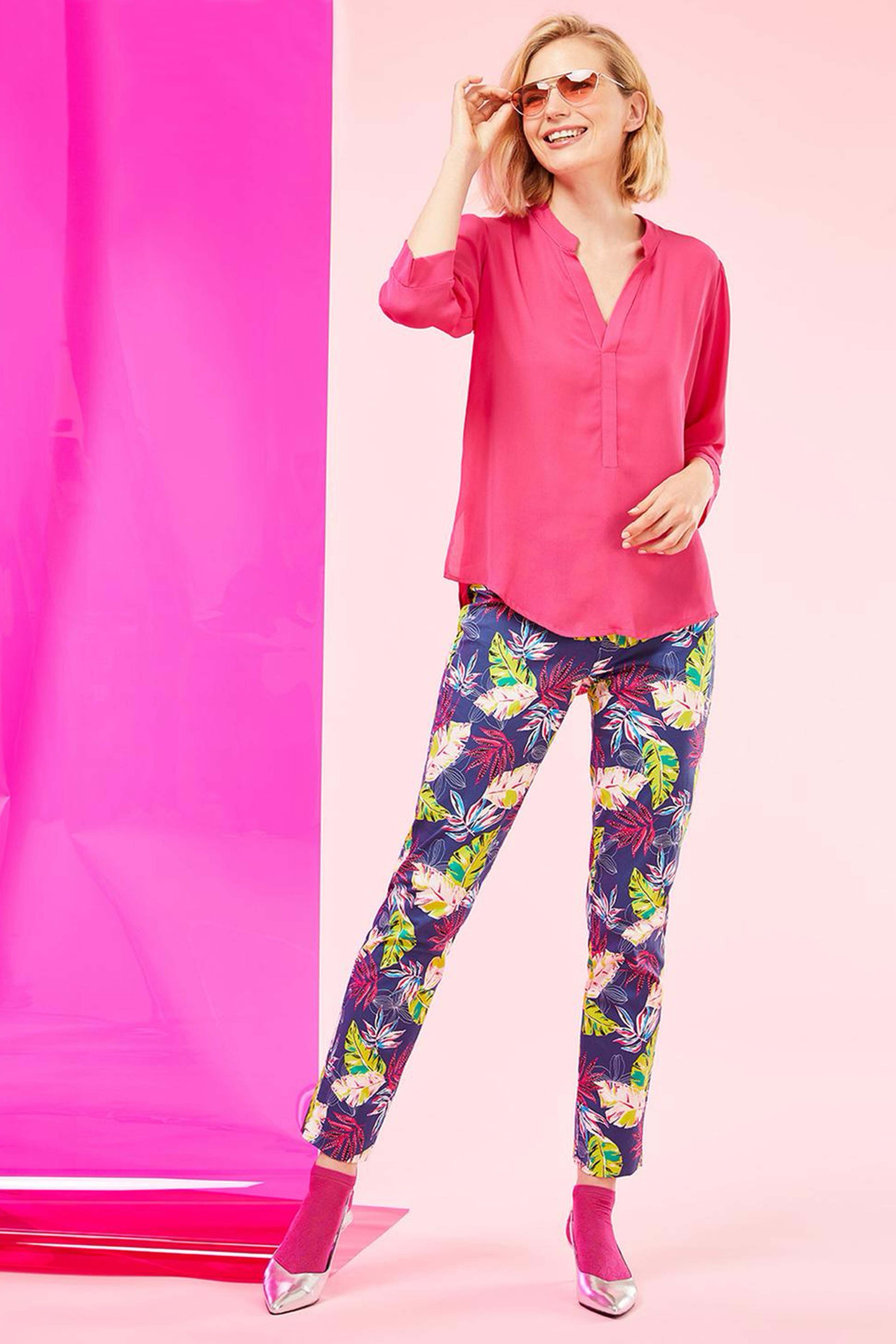 SiSi Tropical Treggings - Navy blue cotton stretch trousers with a tropical leaf style pattern in shades of pink, blue, purple and lime green, button and zipper closures, faux back pockets and side slits on the cuff. Worn with a pink blouse, pink socks and silver shoes.