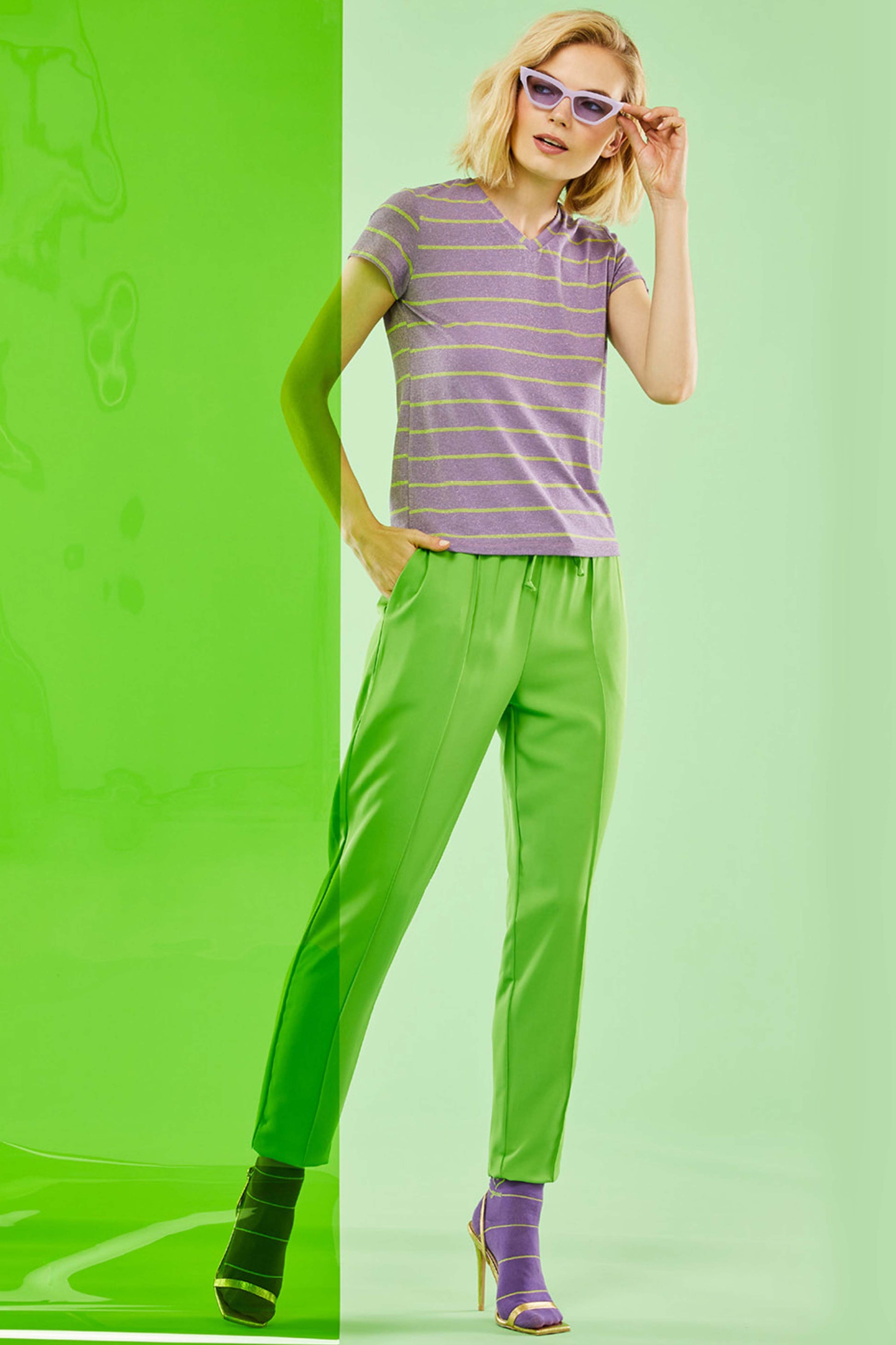 SiSi Swing Trouser - Bright lime green colour jogger style trousers with drawstring waist, side pockets and raised centre seam down the front of the leg. Worn with a purple stripe t-shirt and socks.