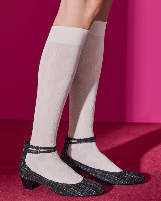 White knee-high socks with a zig-zag pattern worn with black check patterned shoes on a red background