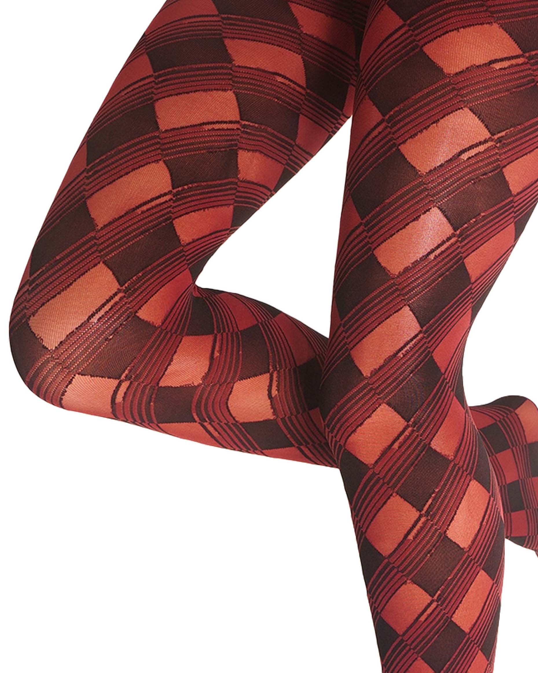A close-up of a person's legs wearing patterned tights with a red, and black harlequin diamond design on a white background.