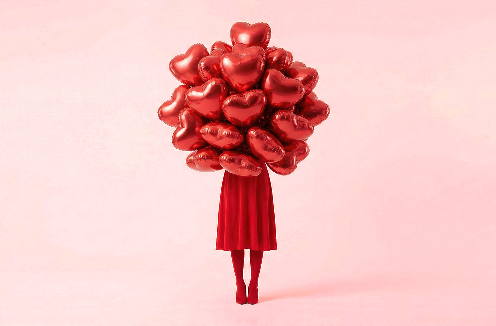 Person holding a large bouquet of red heart-shaped balloons, wearing red skirt, tights and high heels against a pink background