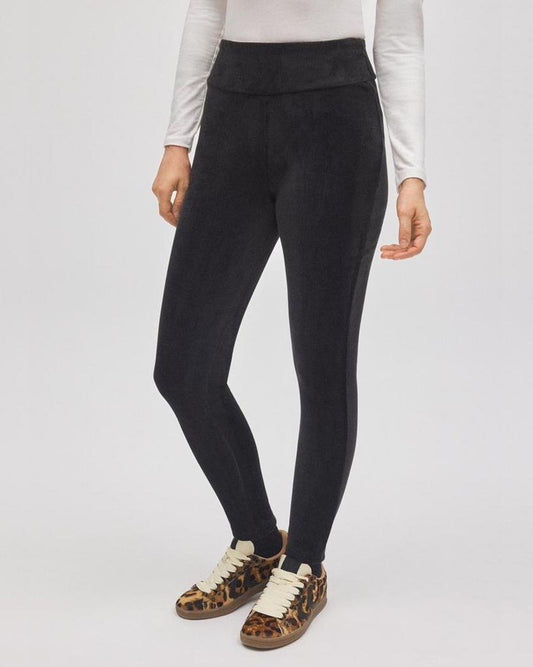 Person wearing black velvet leggings with a white top and brown shoes on a light gray background