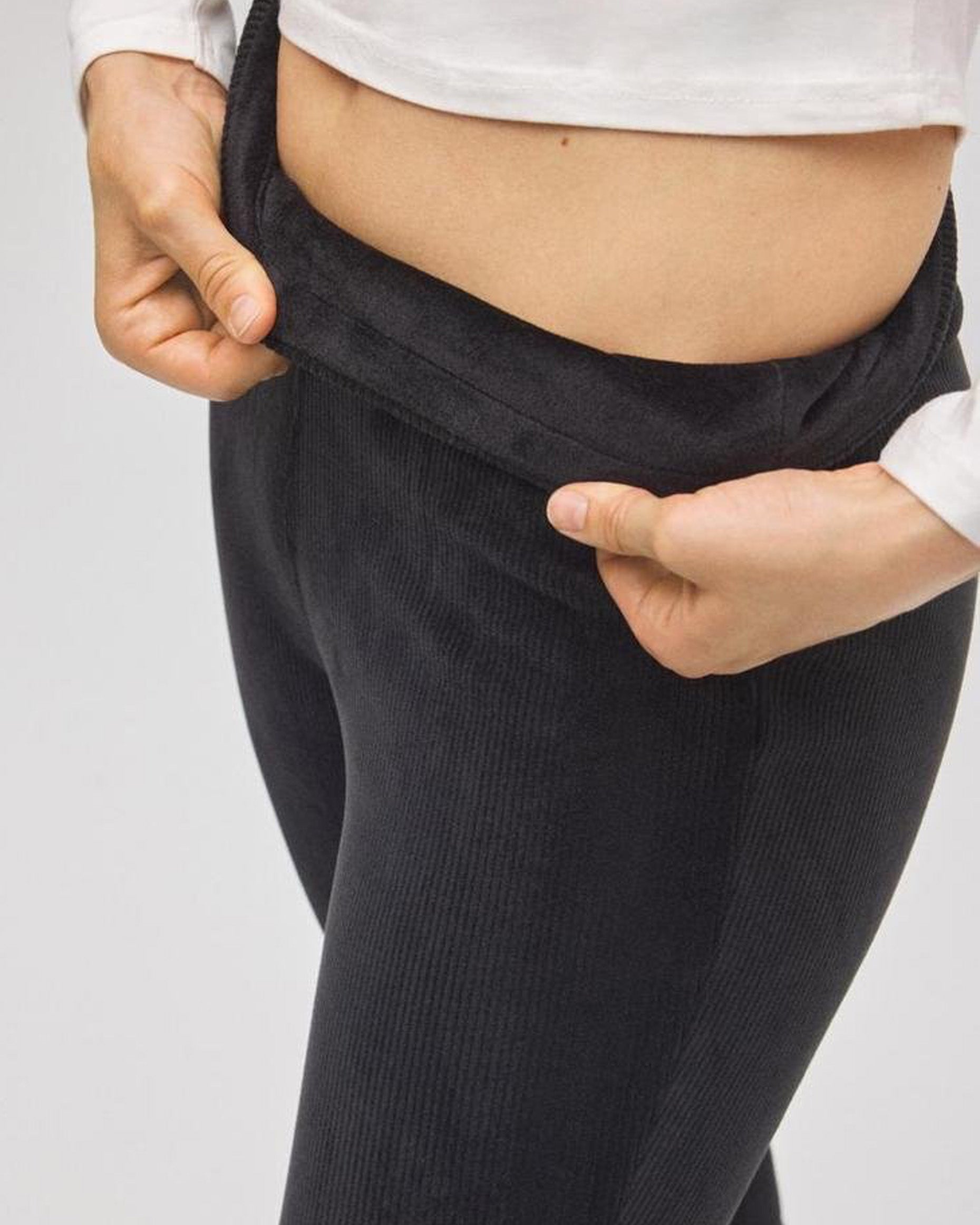 Person wearing black fleece lined cord pants with a white shirt on a light gray background